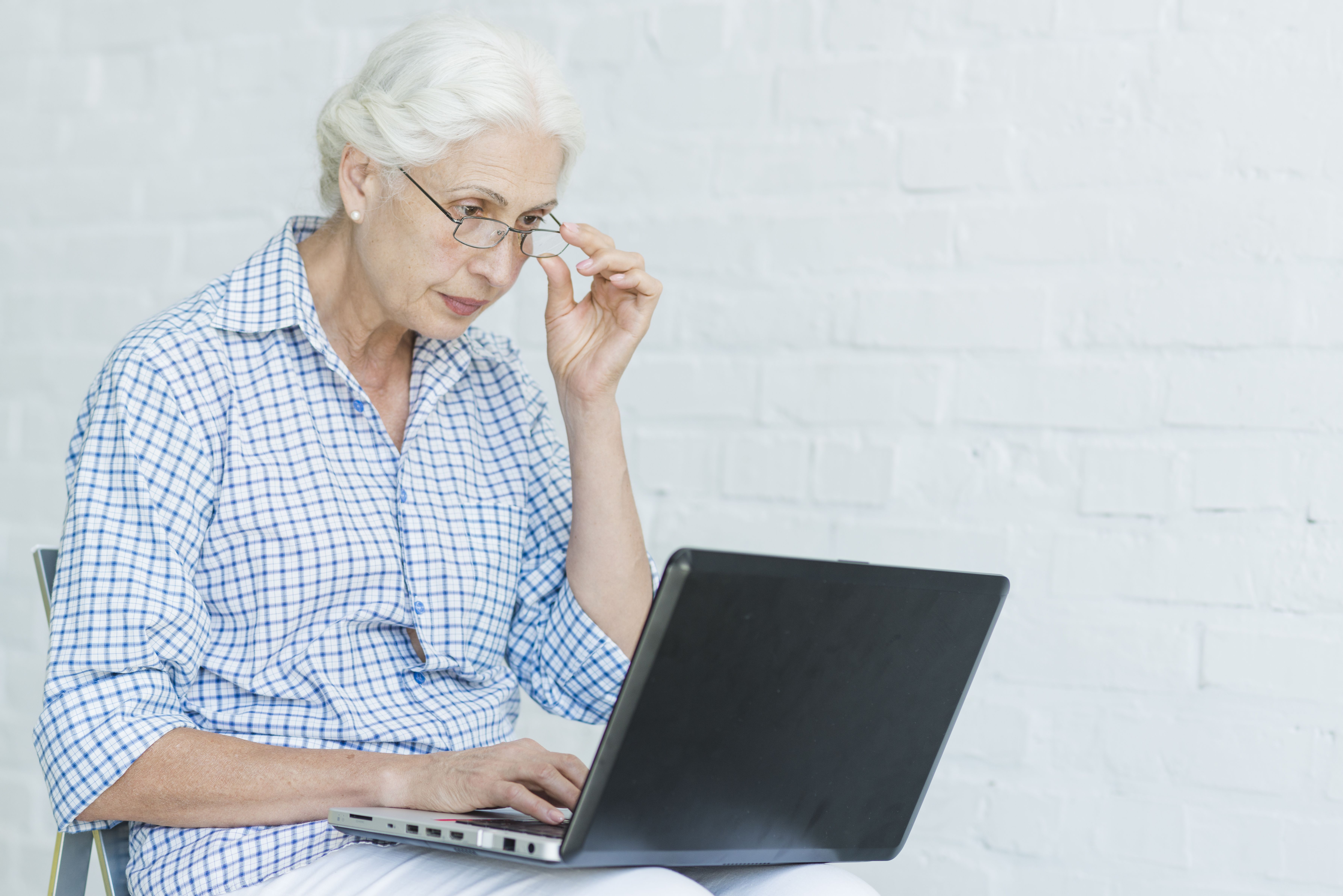 Senior Woman Using Laptop Against White Wall